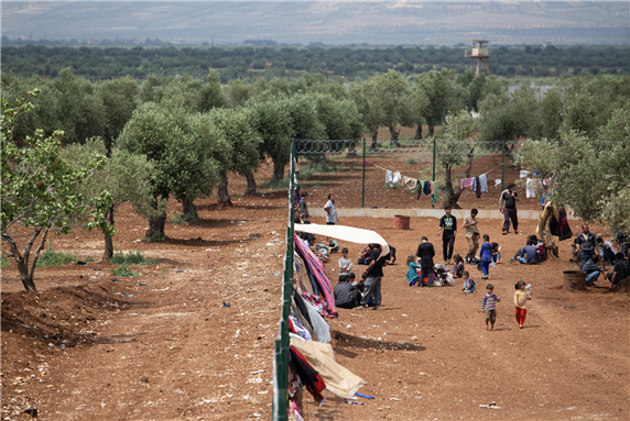 Idlib, Syria - September 30 2016: A refugee camp built under the olive trees. Some of the refugees walking around via Shutterstock